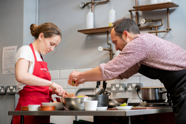 A chef at Brighton Cookery School squeezing lime into a bowl of ingredients.